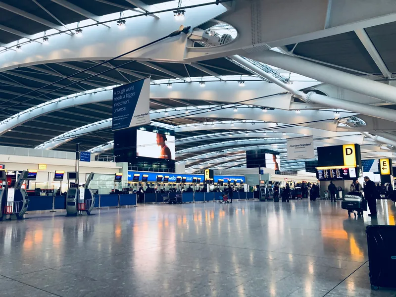Passengers at check-in desks in a bright airport departures hall beneath a curved terminal roof