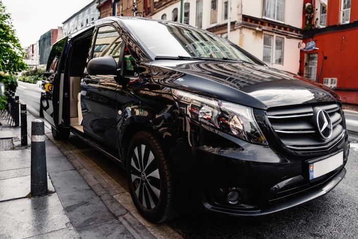 A black Mercedes-Benz V-Class people carrier with its sliding side door open on a wet street