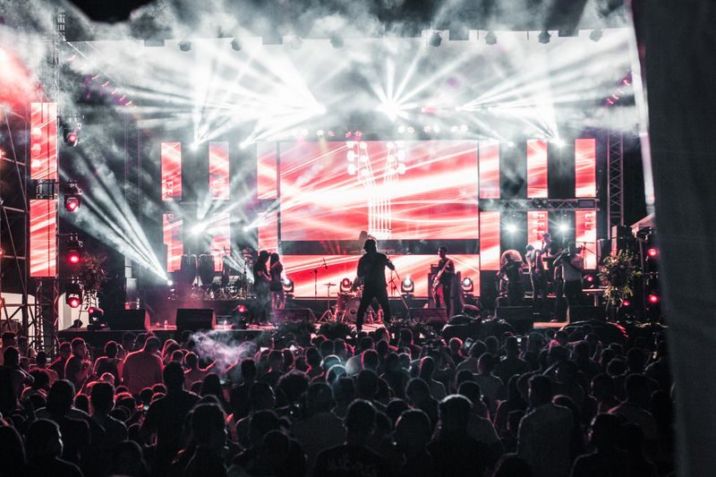 A crowd at a live music event facing a brightly lit stage with large screens